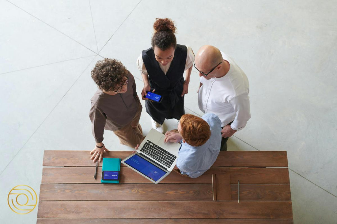 Strategic Leadership in Action - Peas in a Pod: top-down team huddle around laptop and phone, planning next steps together.