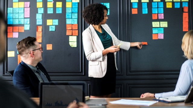 People in room with black board and sticky notes presenting to class/group