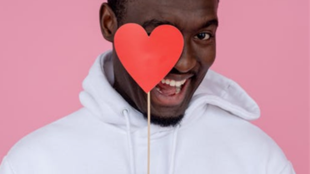 A man with heart shaped on stick holding infront of face and smiling